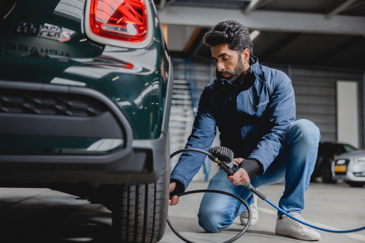 A person in an Alphabet jacket checks and inflates the tire of a car in a well-lit indoor garage.