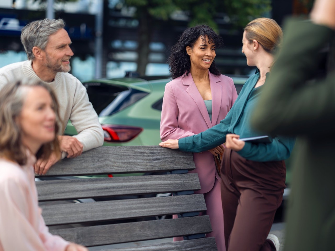 Group of people leaning on a bench talking to each other.