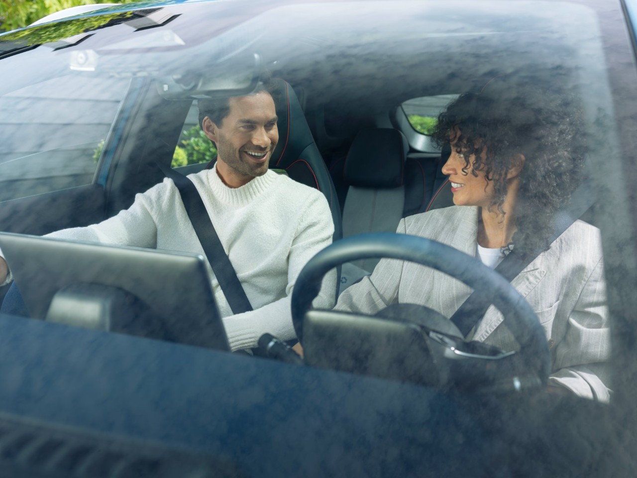 Two people in a car with seat belts, viewed through the windshield.