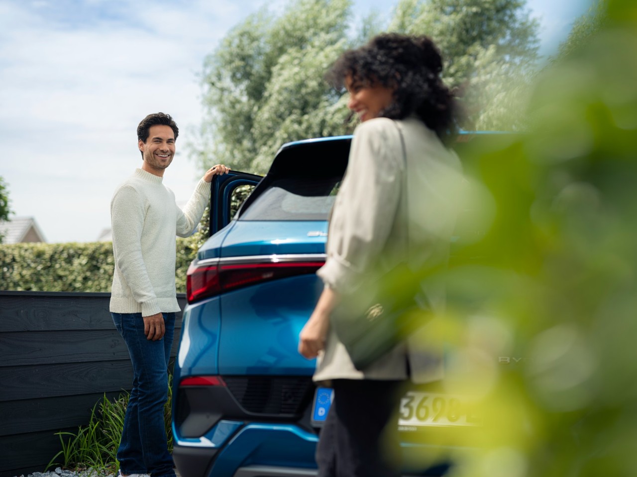 Man opening blue car door. Smiling to woman walking towards him.