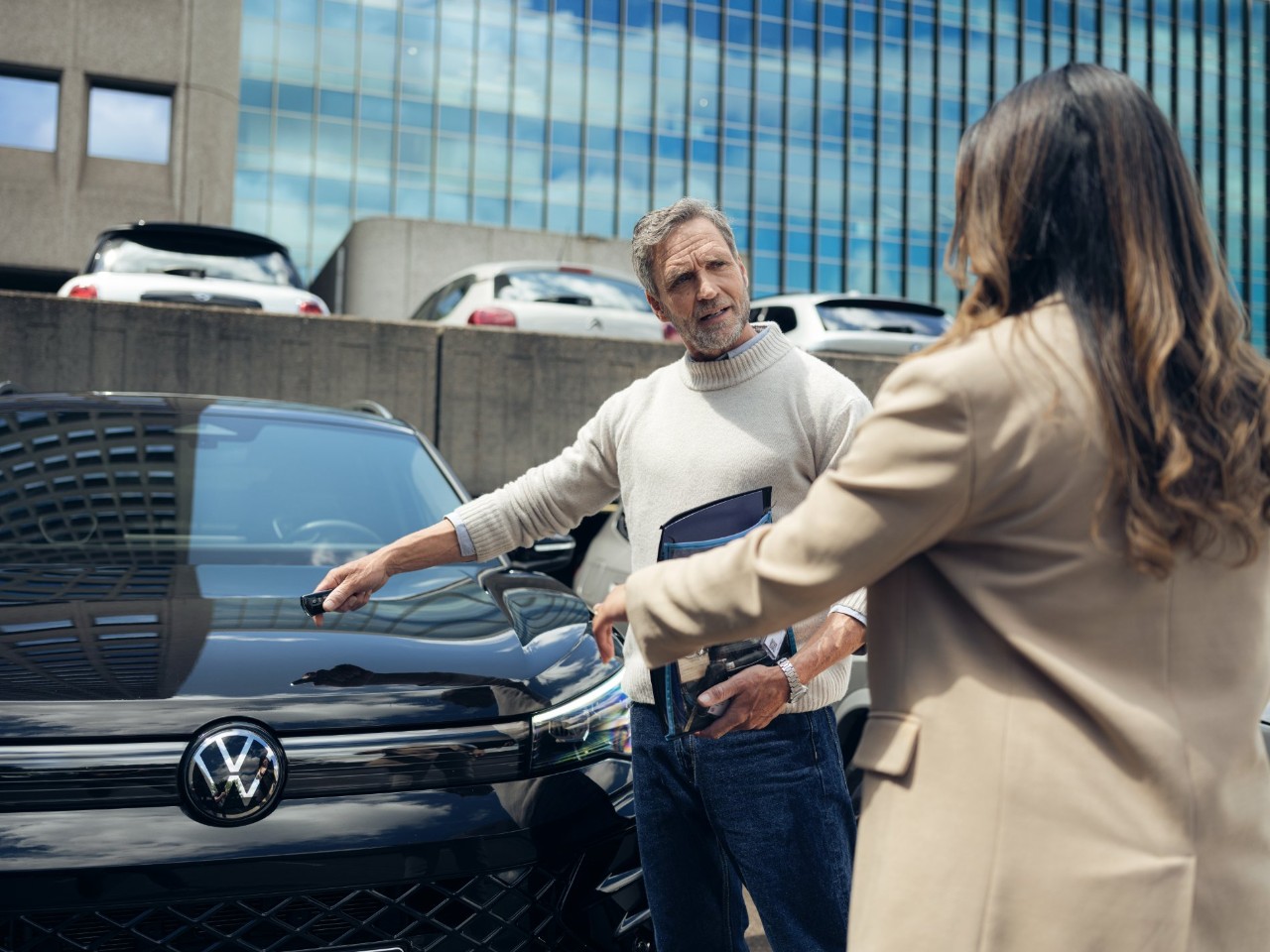 Two people stand next to a Volkswagen. 