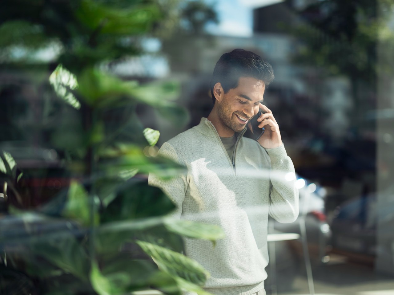 Man talking on a smartphone behind a glass pane.