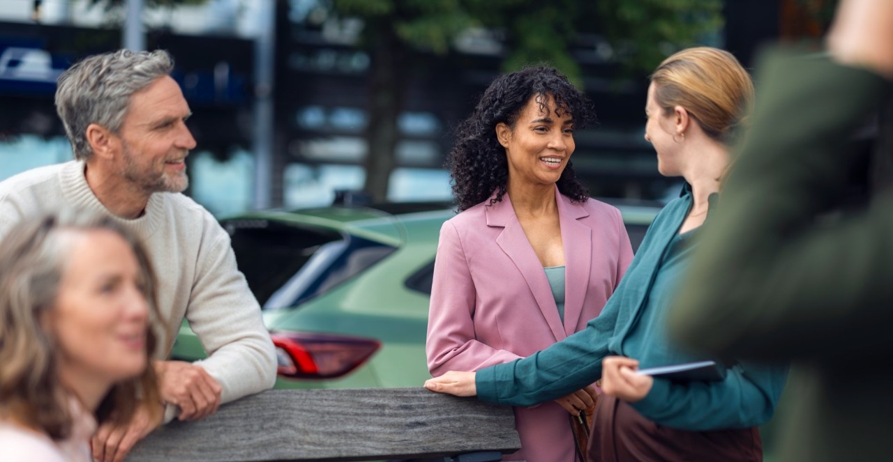 Group of people leaning on a bench talking to each other. 