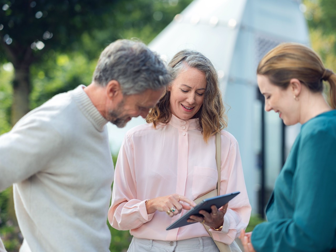 Woman holds a tablet and looks at it together with two other people.