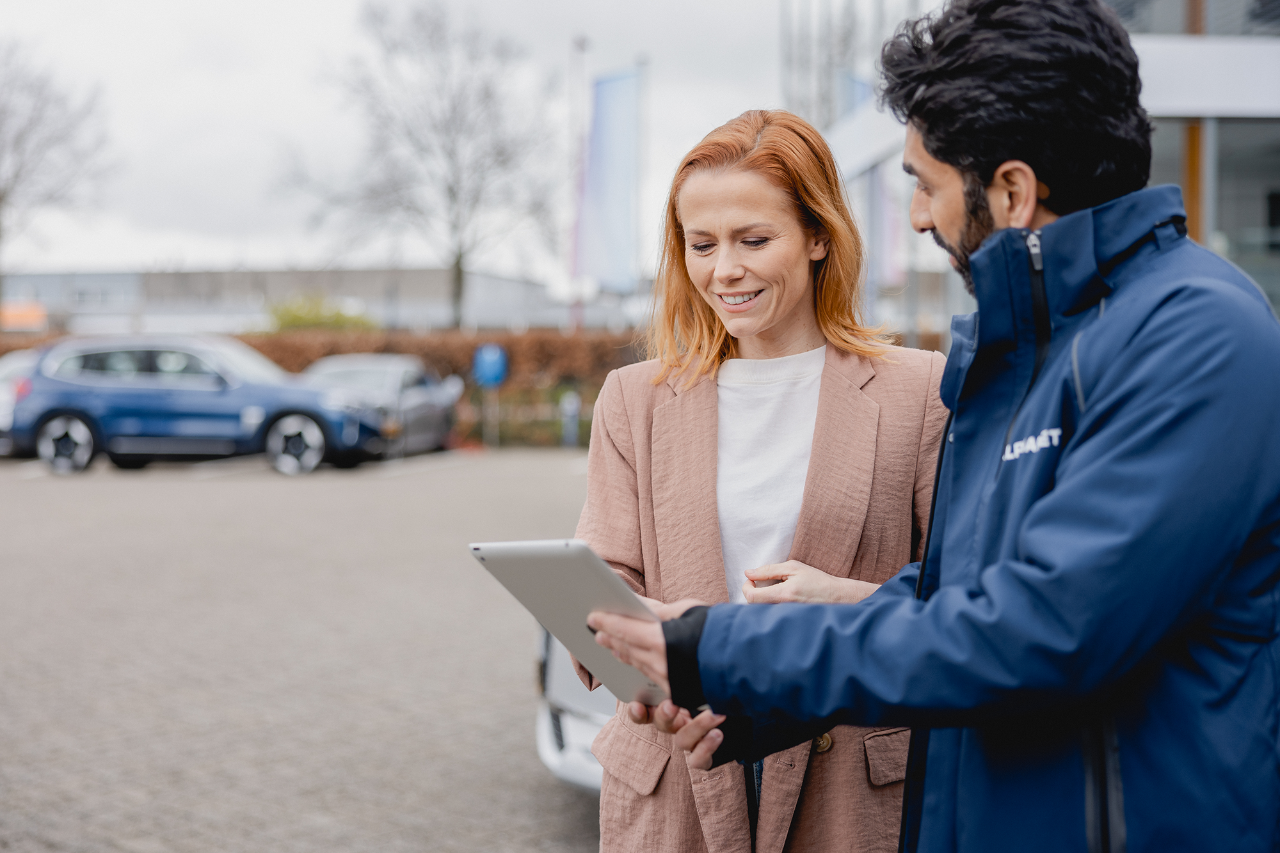 Two people looking at an ipad in front of a car